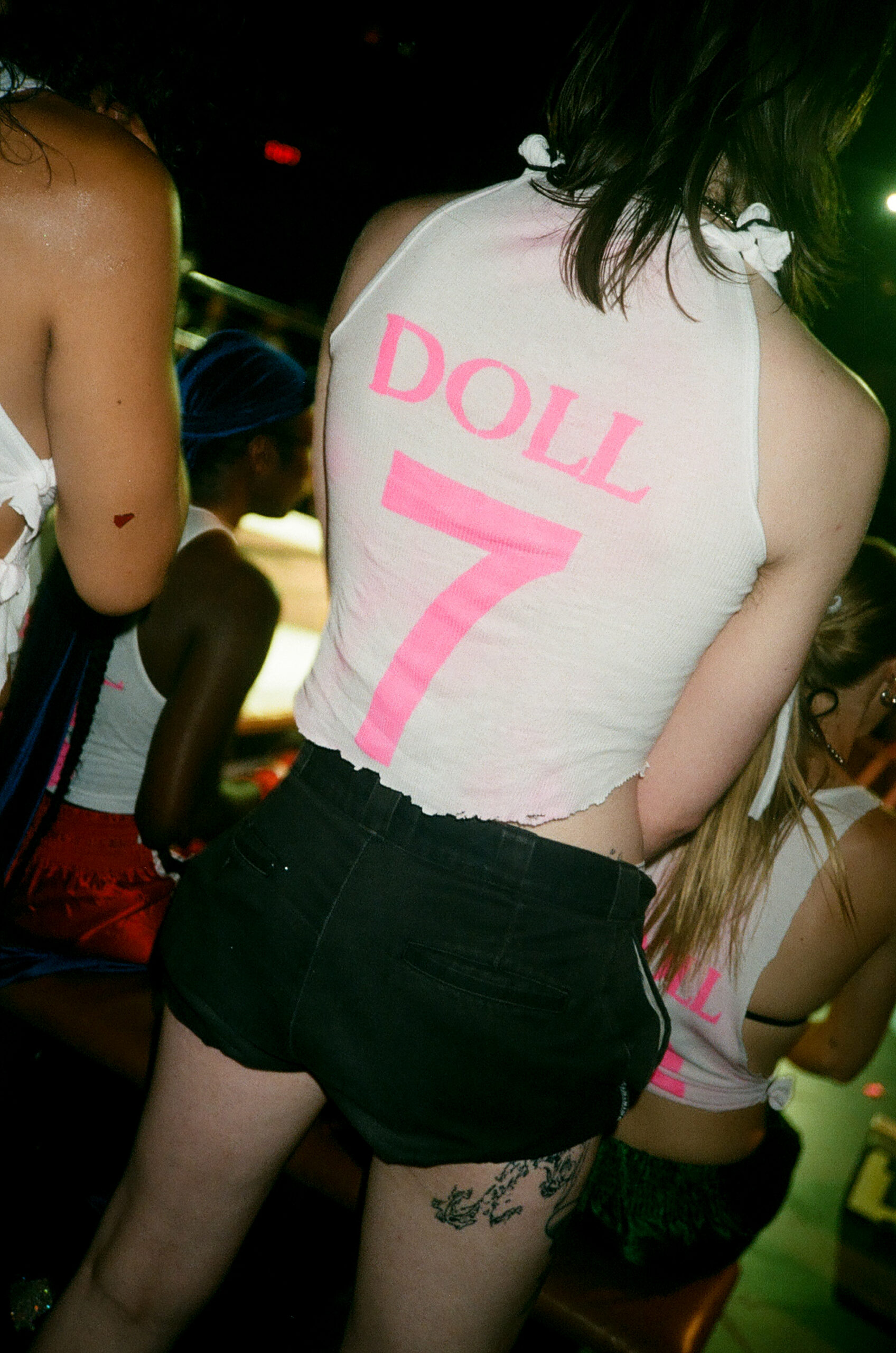 A photo of the back of someone's white tank top that reads Doll 7.