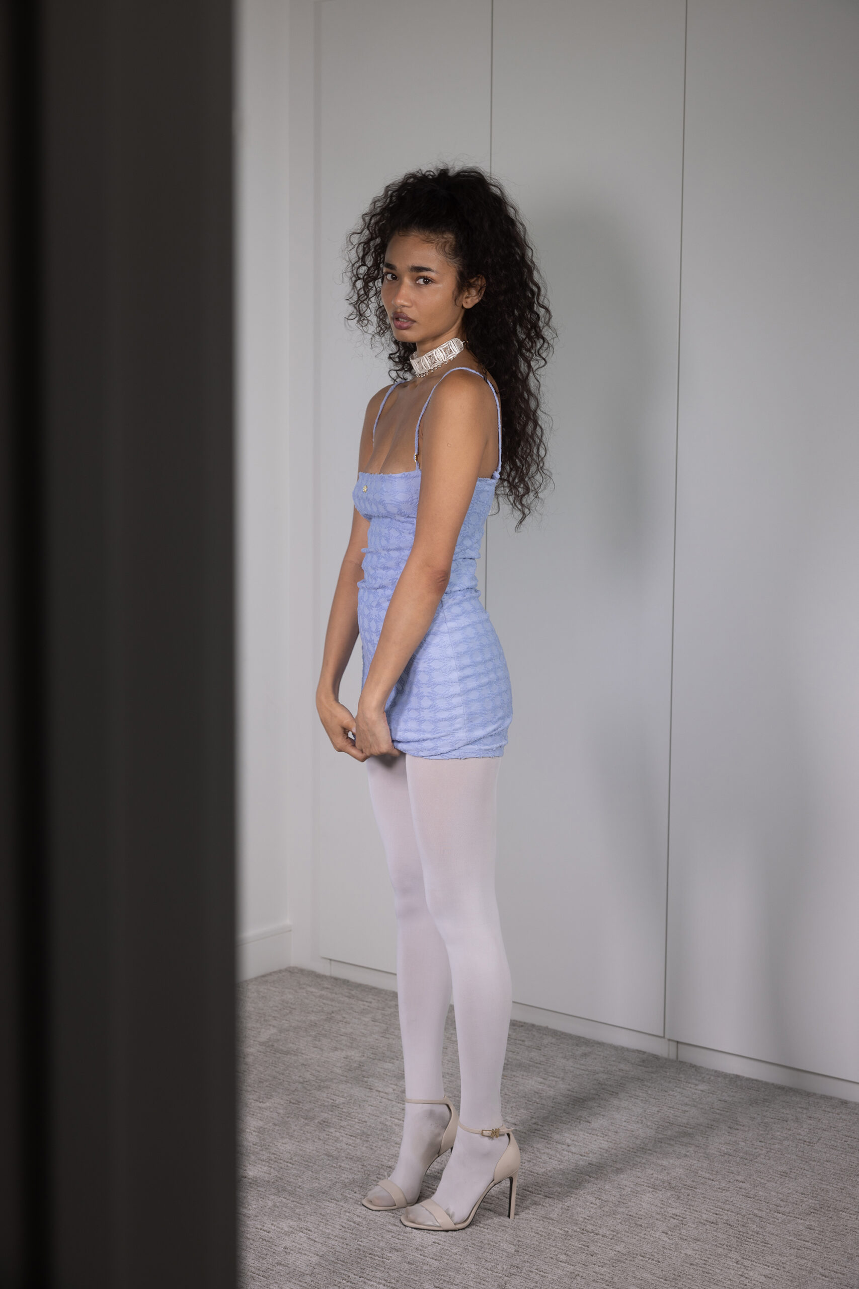 Naisha stands straight gripping the hem of periwinkle dress