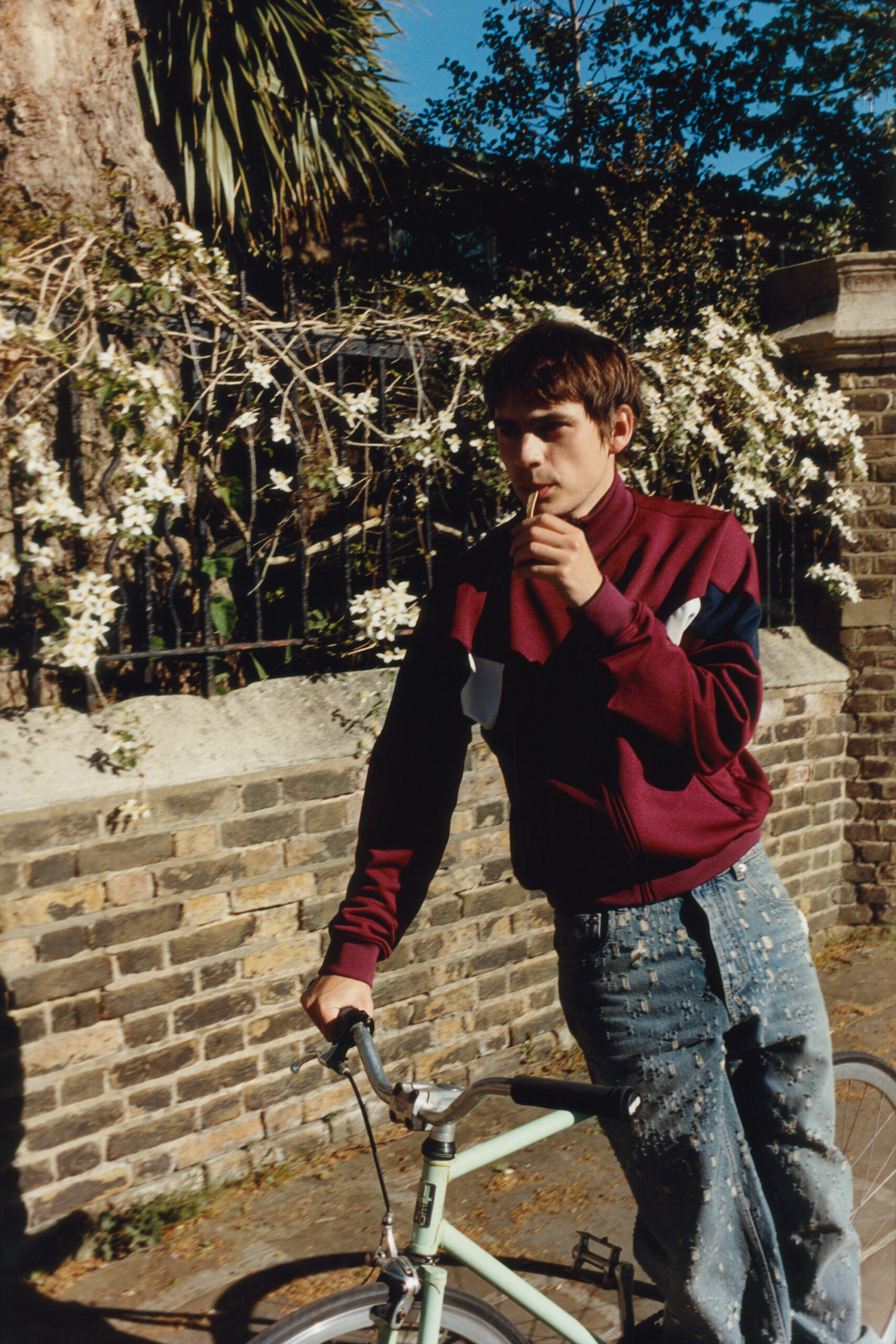 Leans on a bicycle holding a popscicle stick in his mouth