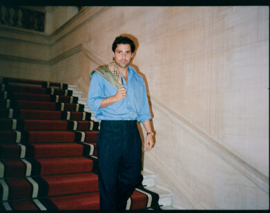 Fabian Frankel going down a red staircase holding a Burberry jacket over his right shoulder