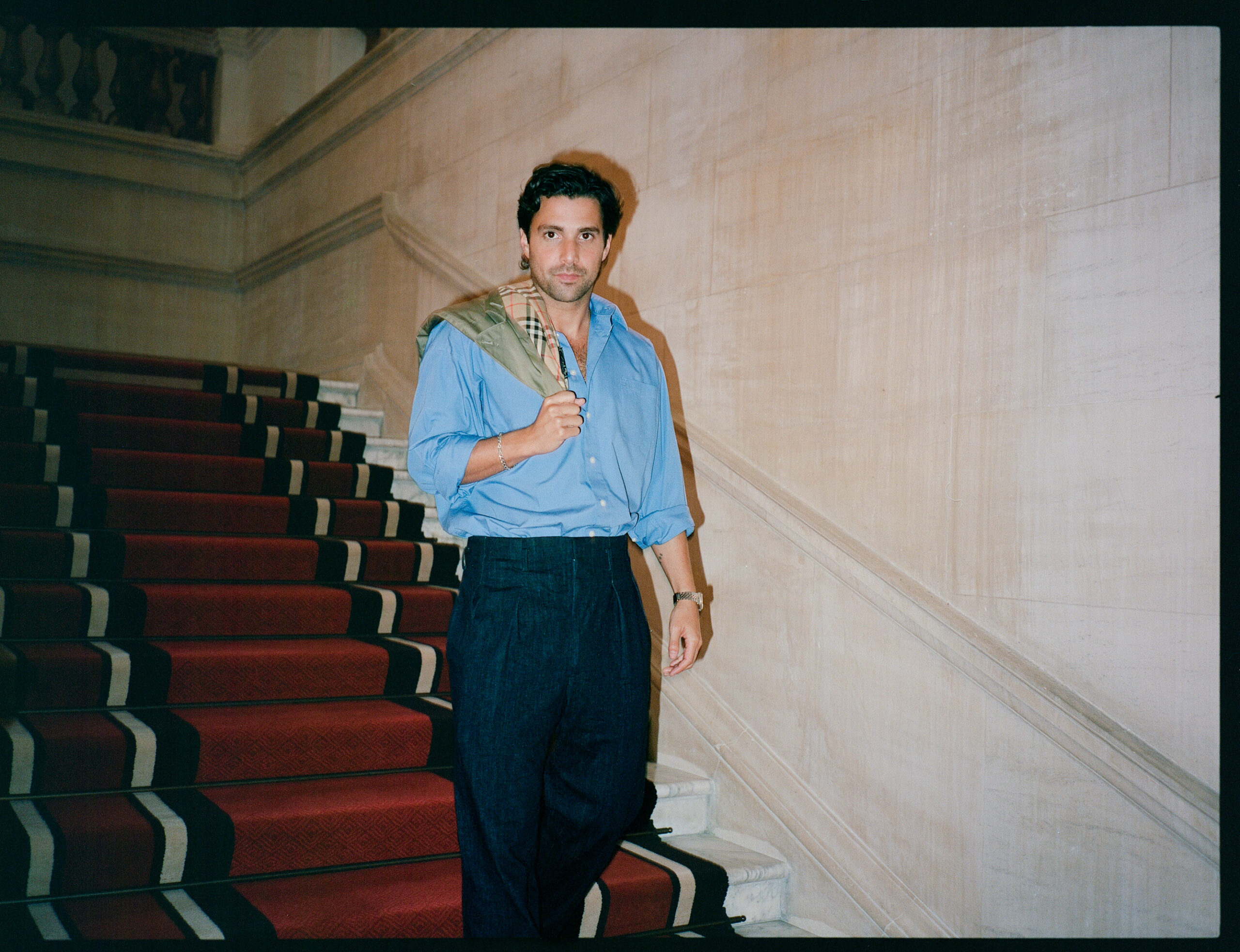 Fabian Frankel going down a red staircase holding a Burberry jacket over his right shoulder