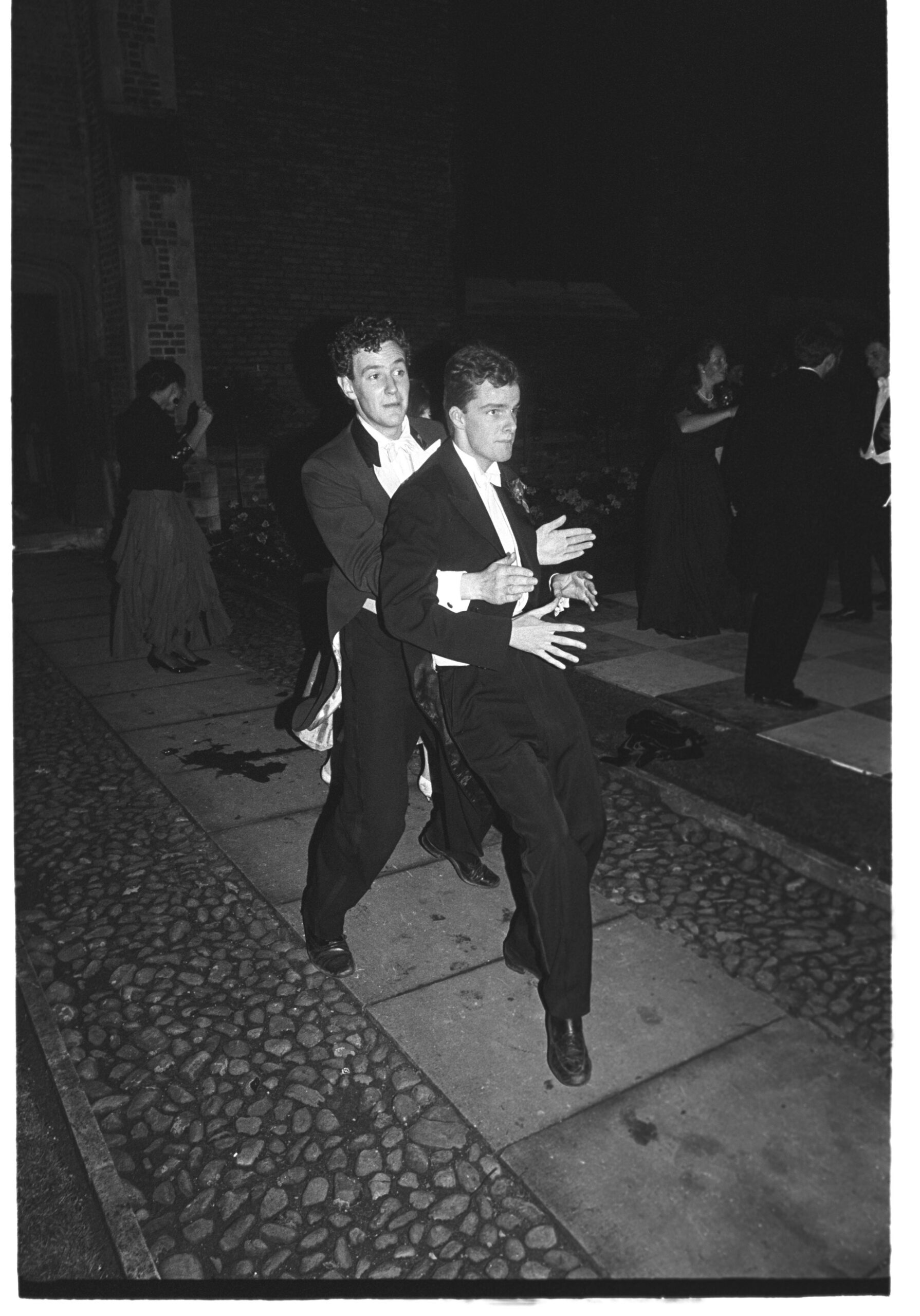 Dominic Armstrong holds Charles Prideaux as they walk on a sidewalk at Cambridge May Ball