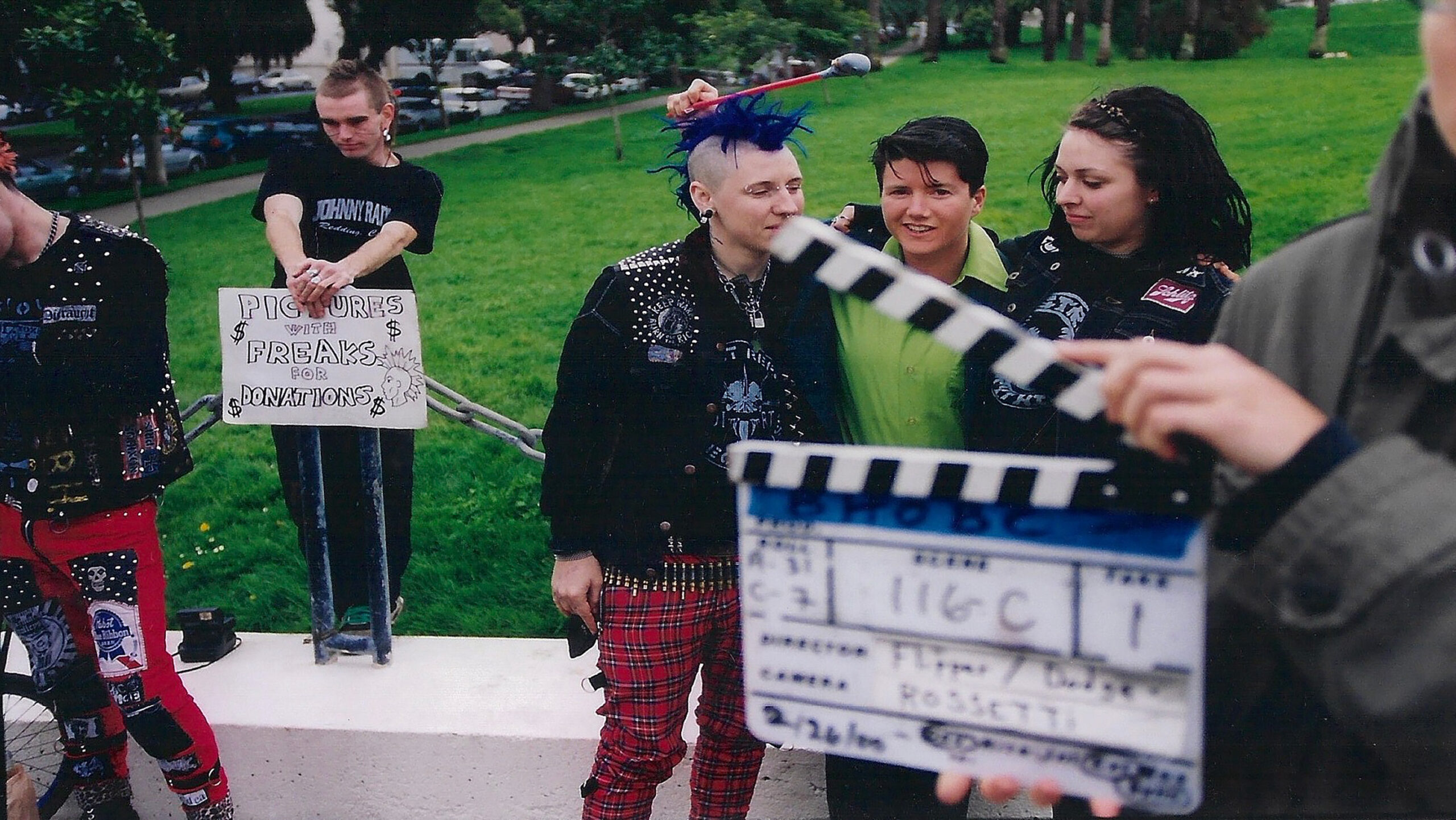 Actors on the set of By Hook or By Crook, standing in front of a green lawn in punk outfits