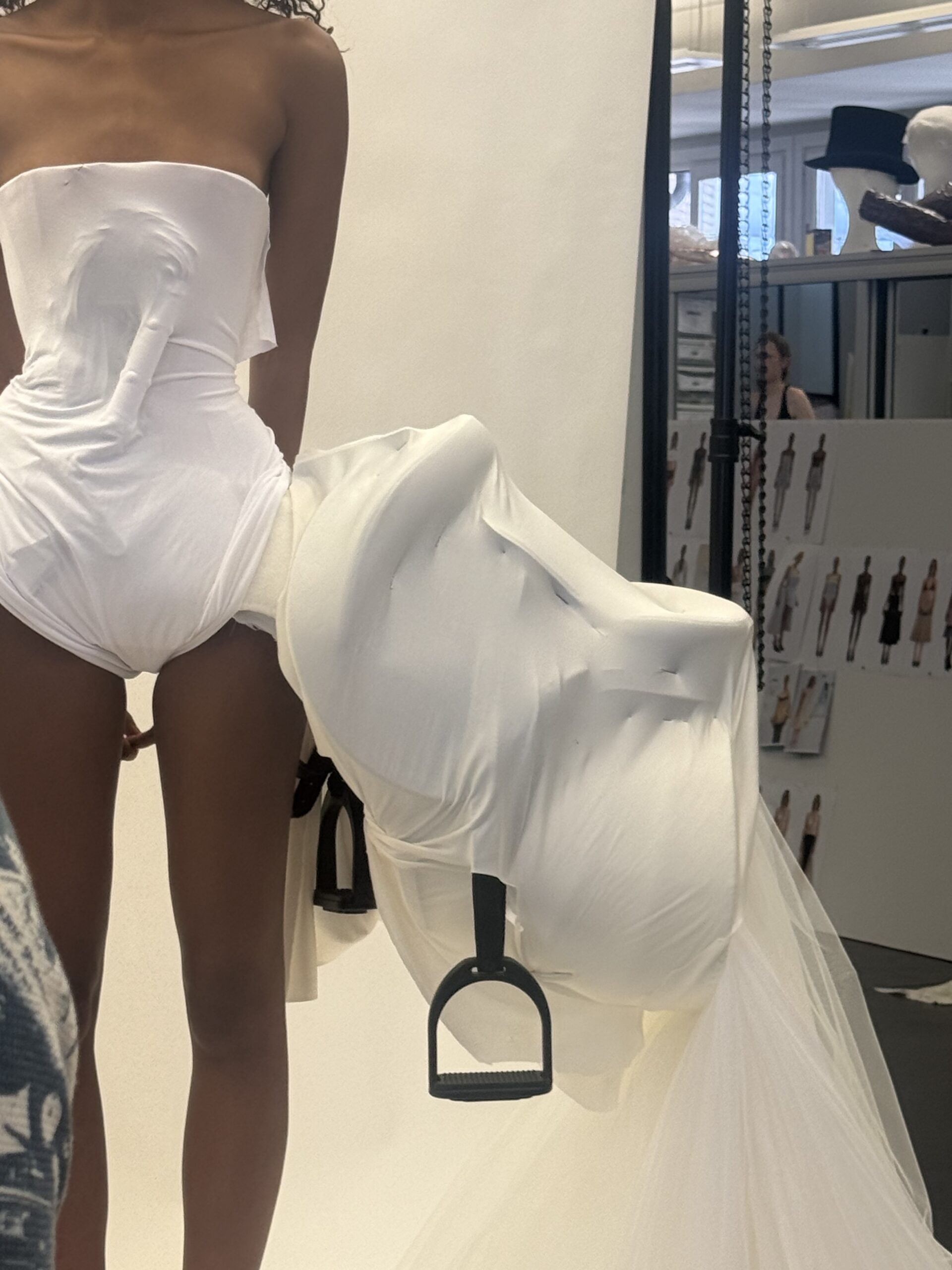 A model wearing a white dress with a large, extended hip piece