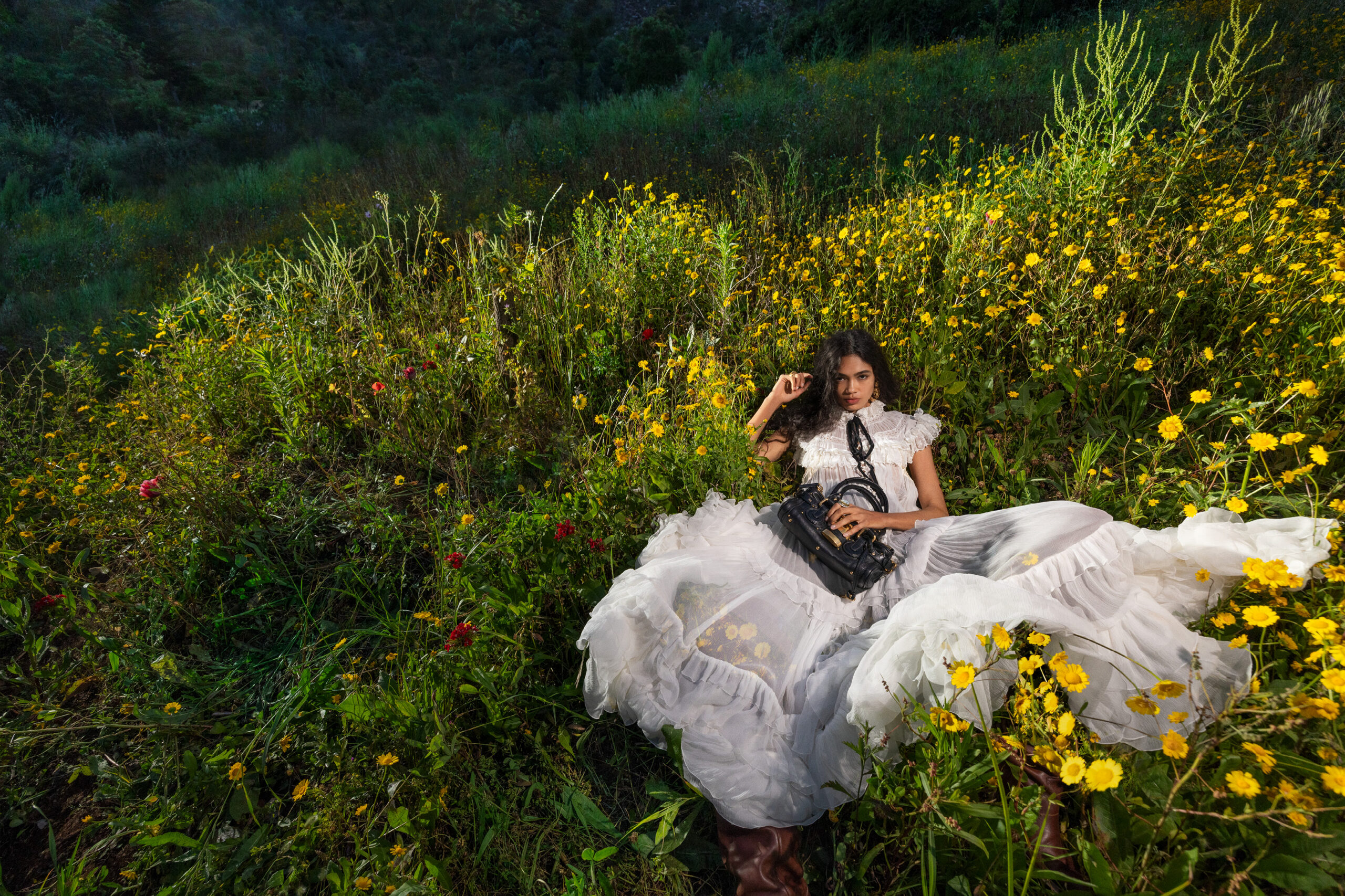 A model lies down in a field of flowers wearing a white Chloe maxi dress.