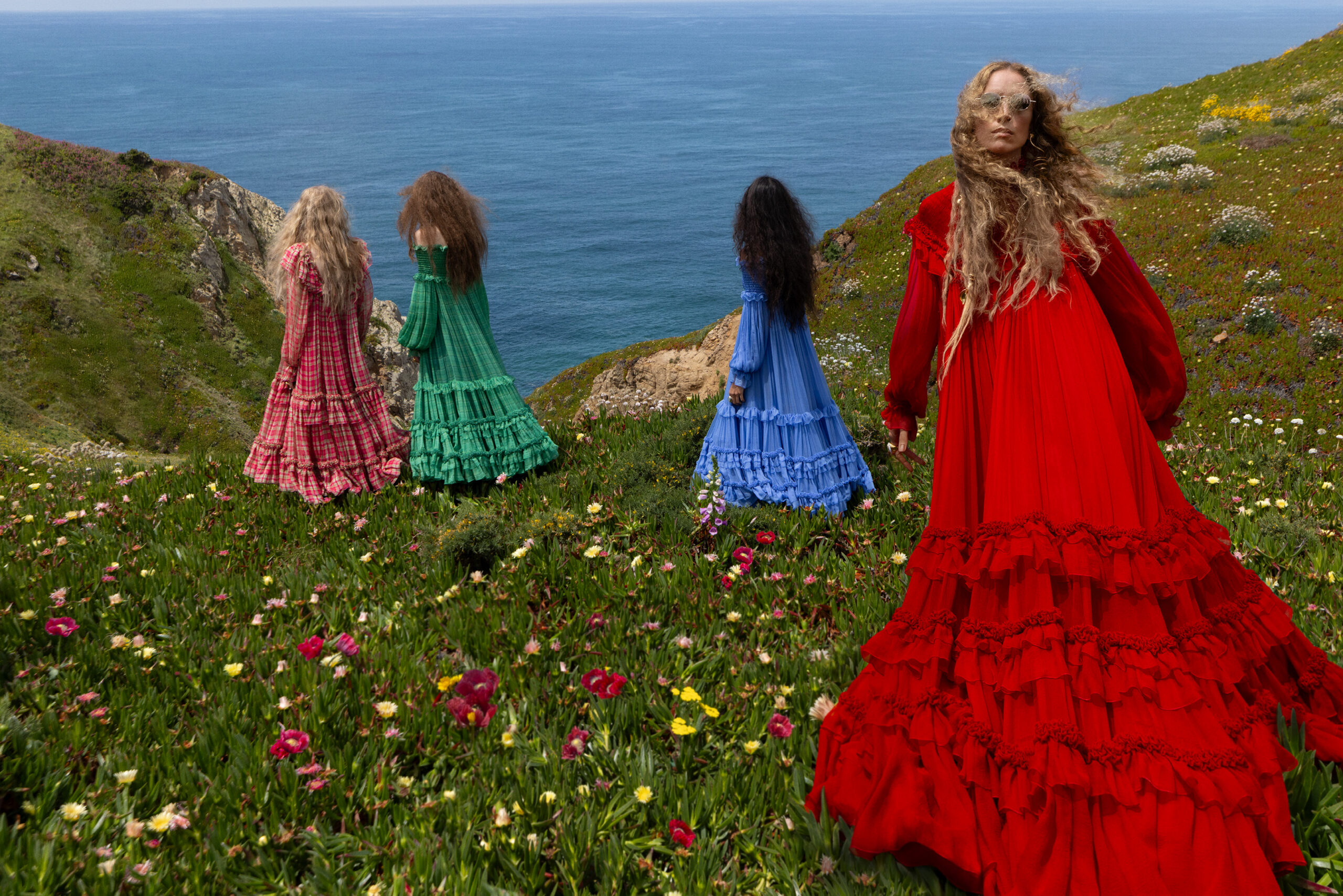 Four models in different colored Chloe gowns on a floral countryside.