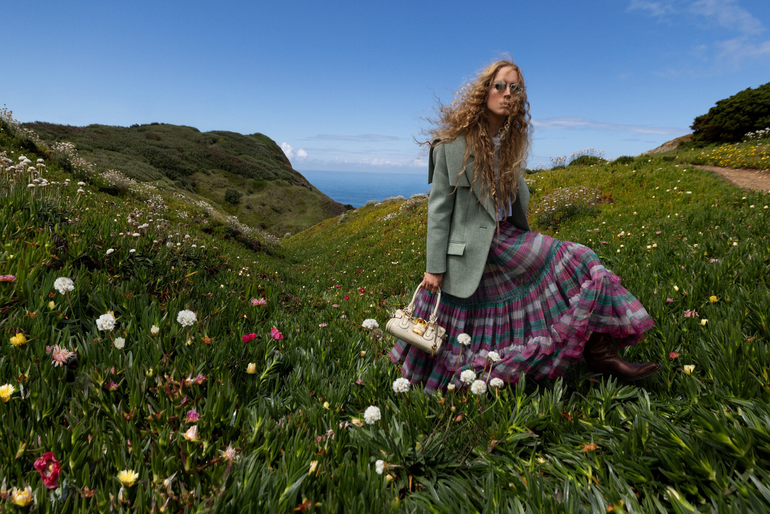 A model wears a Chloe blazer and plaid maxi skirt on a floral countryside.