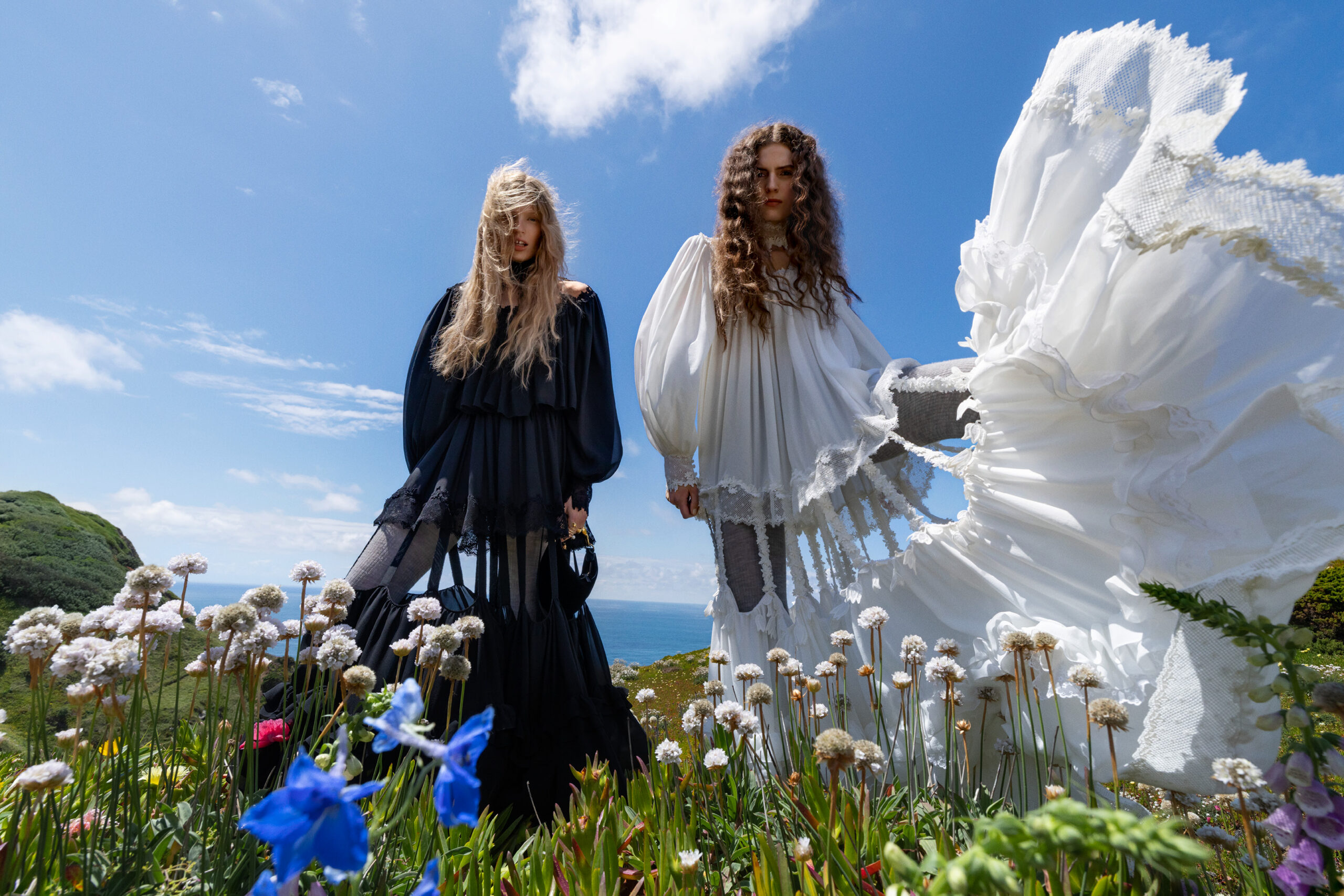 Two models wear silk Chloe maxi dresses in a floral countryside.
