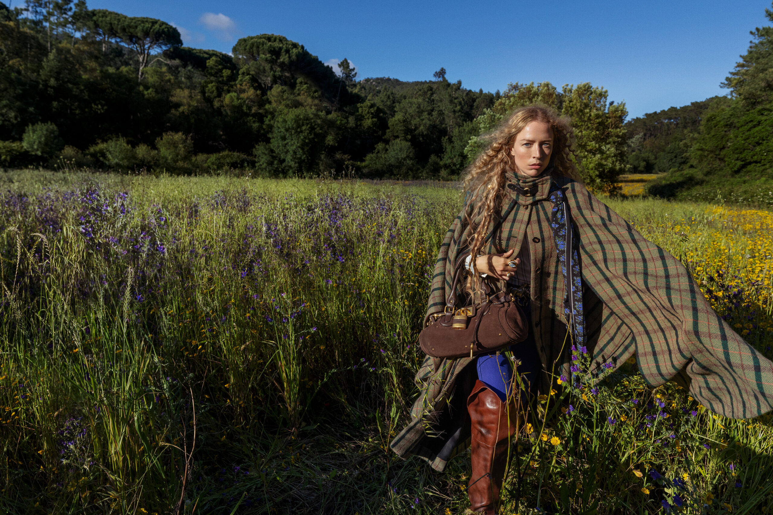 A model poses in a field of grass in a wool plaid Chloe shawl.