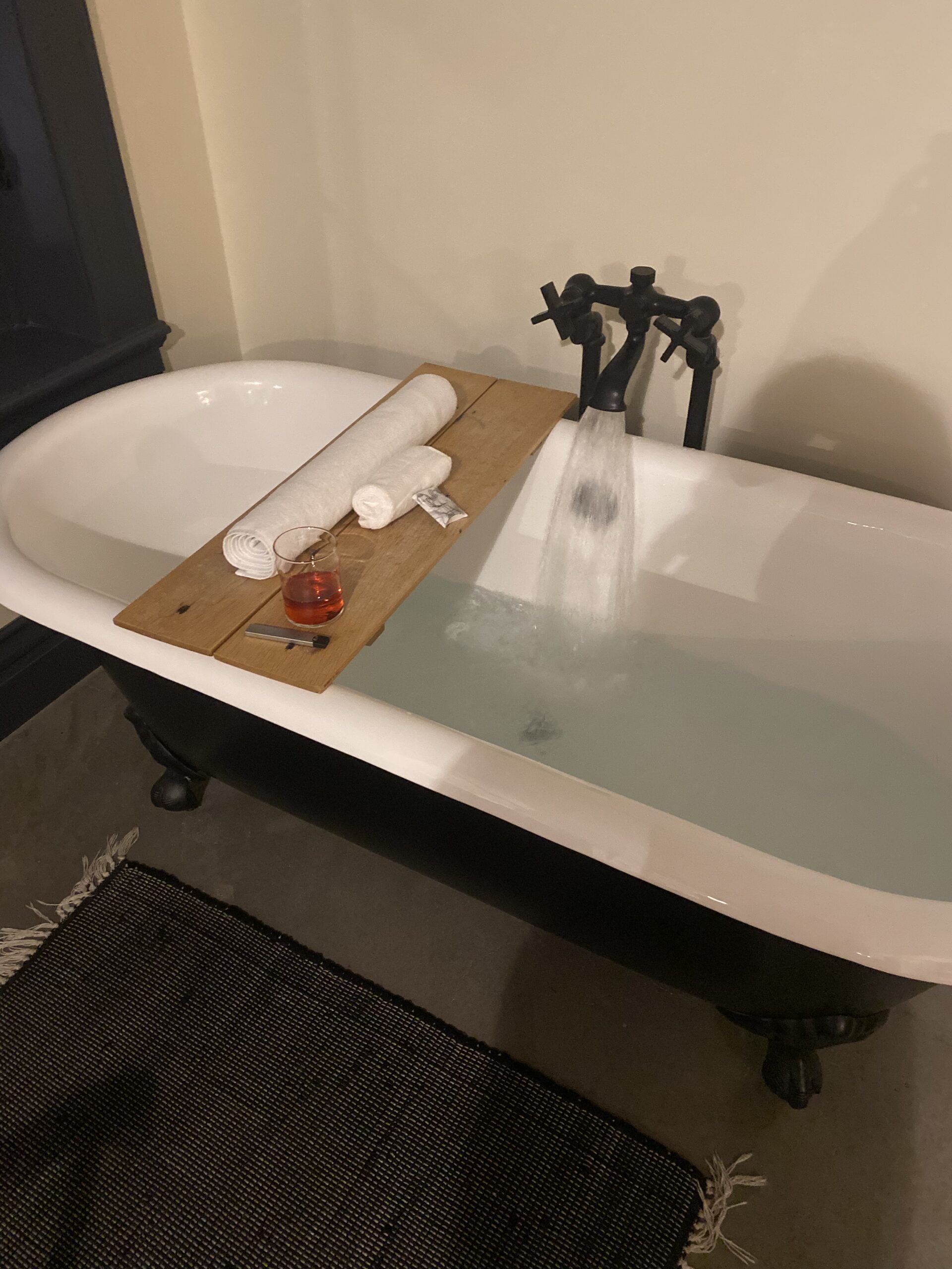 A tub filling up with water. Drink, vape, and towels on top.