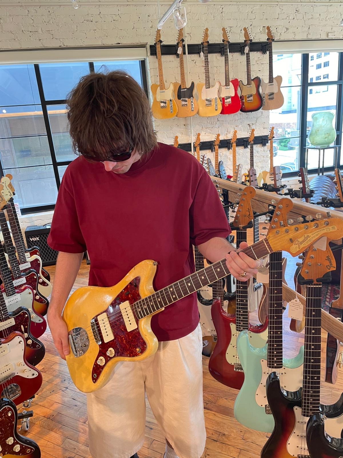 Gene Gallagher of Villanelle stands in a guitar store playing a red and gold electric guitar.