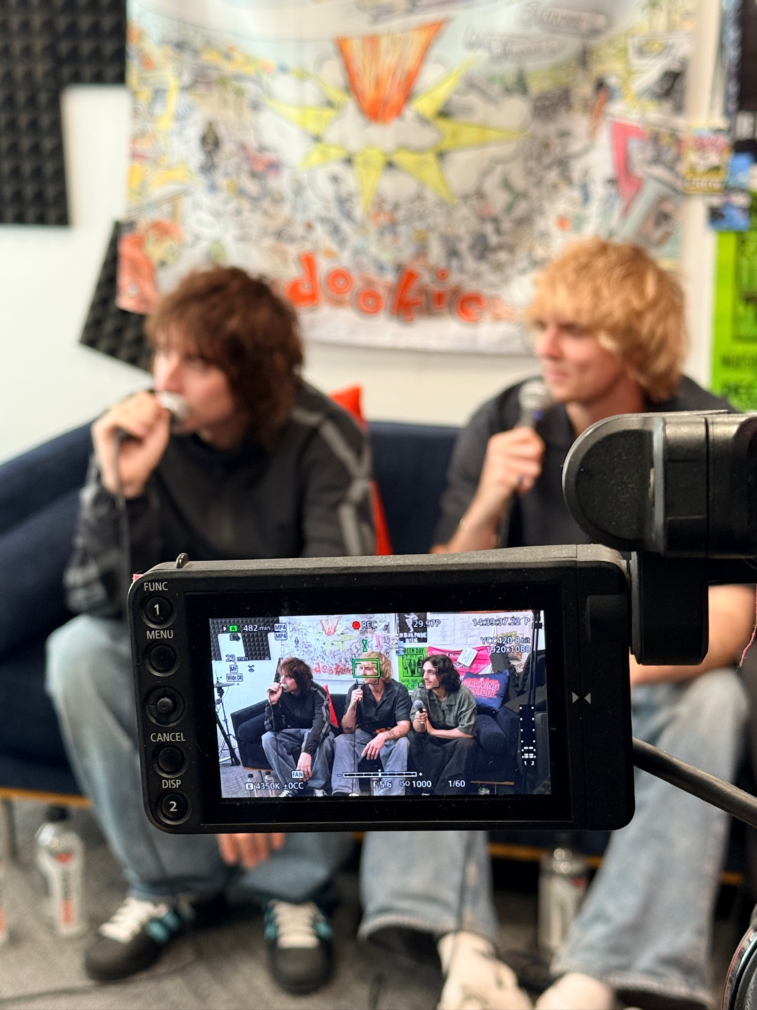 The three members of Villanelle sit on a couch for an interview. We see them through the screen of a video camera.