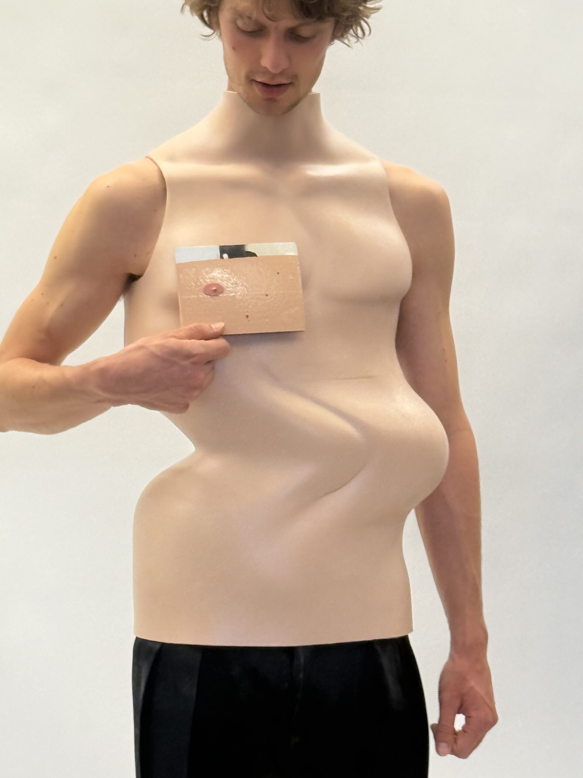A male model wearing a warped torso corset, holding an image of a nipple to his chest
